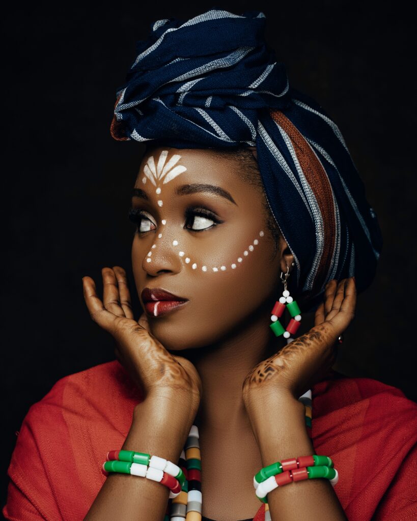 African woman with vibrant headwrap, traditional face painting, and beaded jewelry, exuding cultural elegance.